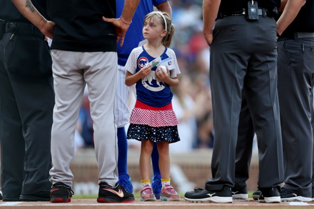 A young girl of a season ticket holder waits beside umpires and coaches from the Chicago Cubs and the Arizona Diamondbacks before meeting Cubs catcher Miguel Amaya at home plate before a game at Wrigley Field in Chicago on July 20, 2024. (Chris Sweda/Chicago Tribune)