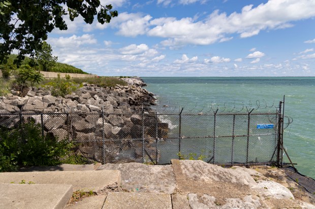 A fence divides Calumet Park and a shoreline dump site at the mouth of the Calumet River on July 18, 2024. (Brian Cassella/Chicago Tribune)