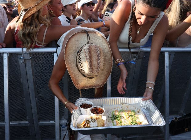 Fans try to balance a tray of food alongside a crowd barrier during a set by DJ Pauly D at the annual Windy City Smokeout outside of the United Center in Chicago on Friday, July 12, 2024. (Chris Sweda/Chicago Tribune)