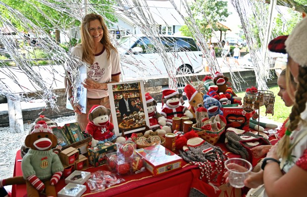 Left, Arlene Okun of Hawthorn Woods, owner and proprietor of monkey business at the Sock Monkey Museum of Long Grove, has a table set up. On right are the Forehand siblings of Highland Park, from left, Dakota, 8, a rising fourth-grader and Kinley, 10, a rising sixth-grader. Taken at Christmas in July at Brothers' Field in downtown Long Grove on July 13, 2024. (Karie Angell Luc/Lake County News-Sun)