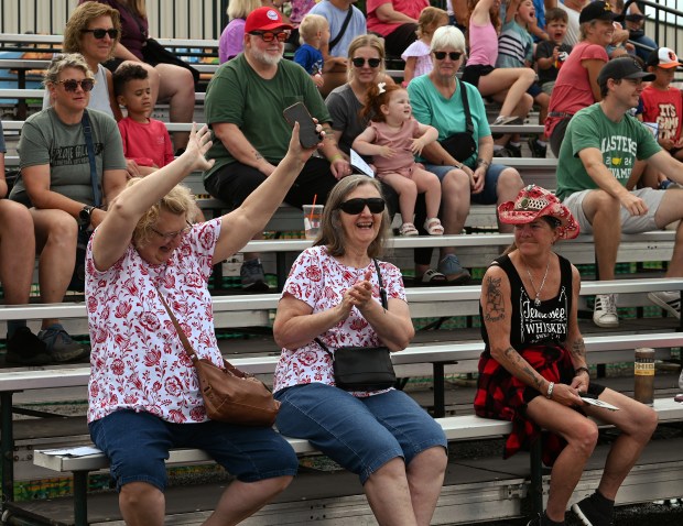 From left, are twins from Lake County. Arms raised in joy for being picked as a possible prize recipient in the for-adults-only third round of the Show Me Swine Pig Races is Carol Loui of Lake Villa. Loui's twin, in the same shirt pattern, is Sandra Llanes of Round Lake. Carol Loui did wind up winning a prize of a bracelet that Loui gave to a child Taken at the July 24, 2024 Wednesday opener of the Lake County Fair in Grayslake. (Karie Angell Luc/Lake County News-Sun).