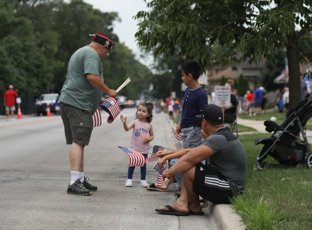 Shawn Schrader hands out flags to spectators prior to a Fourth of July parade in Elmwood Park on Thursday, July 4, 2024. (Trent Sprague/for the Pioneer Press)