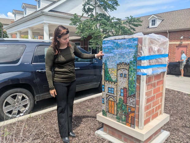 Meghan Maple, associate executive director of Smith Village, props a mosaic on a brick time capsule in front of the facility in Chicago's Beverly community. After it is filled with predictions from Smith Village residents, the capsule will be sealed and decorated with four mosaics. It's planned to be opened in 2074. (Janice Neumann/Daily Southtown)