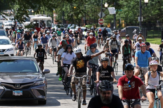 A bicyclist signals for a left turn as the fourth annual Bronzeville Bike Tour rides north in the 3300 block of South Indiana Avenue on July 30, 2022, in Chicago. A pre-tour program was held prior to commemorate the Chicago Race Riot of 1919. (John J. Kim/Chicago Tribune)