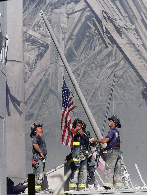 Brooklyn firefighters George Johnson, from left, of Ladder 157, Dan McWilliams, of Ladder 157, and Billy Eisengrein, of Rescue 2, raise a flag at the World Trade Center in New York on Sept. 11, 2001. (Thomas E. Franklin/Bergen County Record)