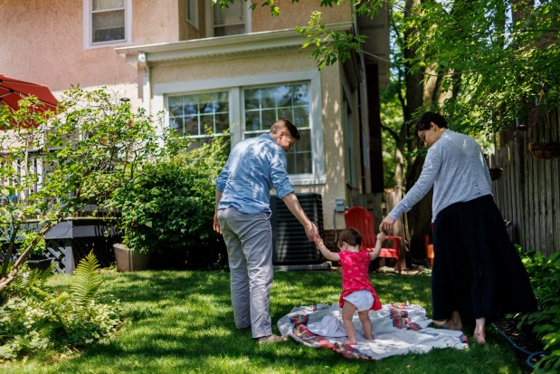 The Rev. Britt Cox, 39, left, and Jessica Hager, 38, walk in their backyard with their 1-year-old daughter, Luca, at their Evanston home on June 27, 2024. Cox serves as executive pastor at First United Methodist Church in Evanston. (Armando L. Sanchez/Chicago Tribune)