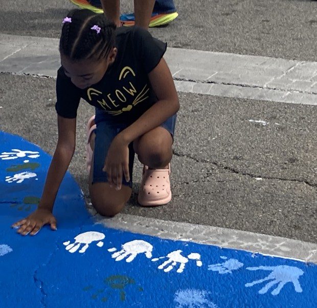 A youngster places her handprint on the crosswalk mural. (Steve Sadin/For the Lake County News-Sun)