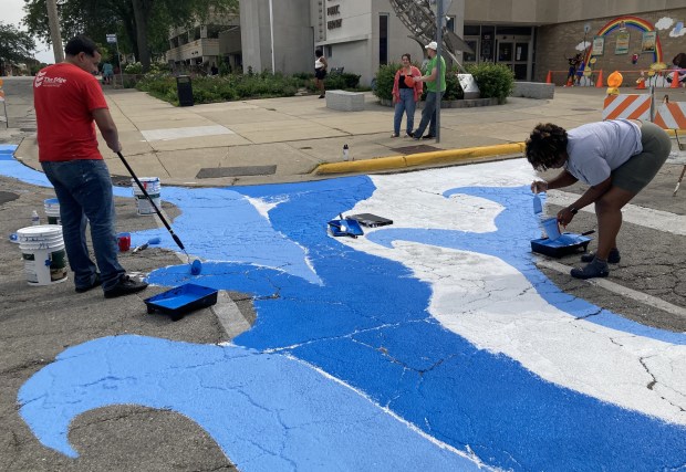 Volunteers paint the backdrop for the crosswalk mural. (Steve Sadin/For the Lake County News-Sun)