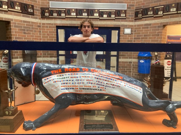 Senior linebacker Mikey Claycombe poses with some of the Oswego football program's state trophies and mascot before practice on Tuesday, Aug. 20, 2024. (Rick Armstrong / The Beacon-News)