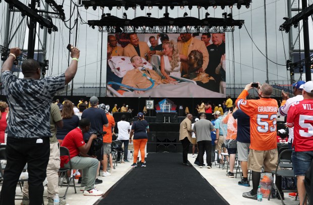 Steve McMichael, with his wife Misty and former teammates, are displayed on the video board as he is inducted into the Pro Football Hall of Fame during the enshrinement ceremony at Tom Benson Hall of Fame Stadium on Aug. 3, 2024, in Canton. (John J. Kim/Chicago Tribune)