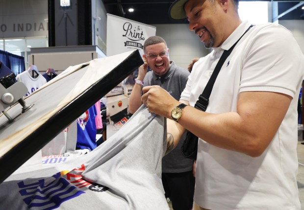 Vince Rainey, center, jokes around with vendor Imanuel Basley, right, as he prints one of his custom Hope Vs Haters t-shirt in his booth, The Print Lounge, in the DemPalooza exhibition at McCormick Place on Aug. 20. 2024. (Stacey Wescott/Chicago Tribune)