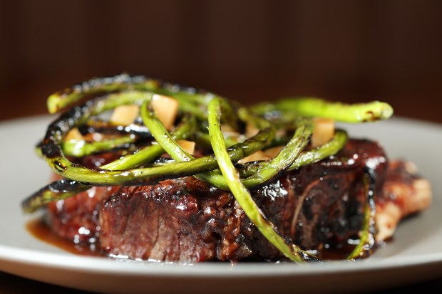 The 16-ounce bone-in, cowgirl cut ribeye steak topped with charred garlic scapes at John's Food and Wine. (Terrence Antonio James/Chicago Tribune)