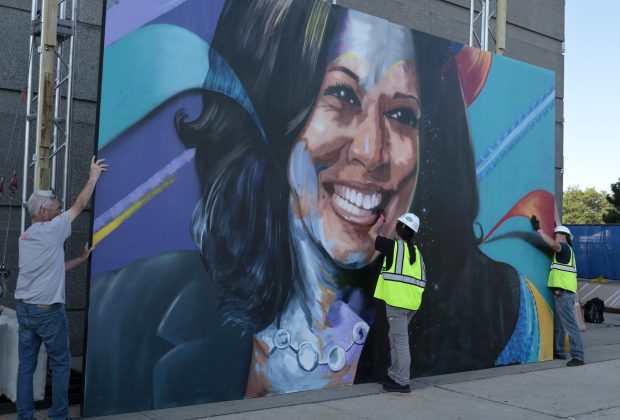 Local Union 1 Carpenter Jaclyn Ramirez, center, puts up a large mural of Vice President Kamala Harris outside the United Center with other carpenters along Madison Street on Aug. 16, 2024, in Chicago. (Antonio Perez/Chicago Tribune)