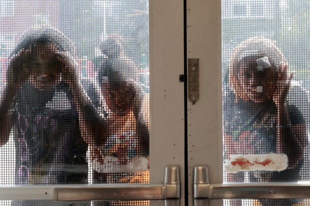 Parents and caregivers peer through the entry doors as they say good-by to their children on their first day back to school at Chalmers Elementary Specialty School on Monday, Aug. 26, 2024. (Antonio Perez/Chicago Tribune)