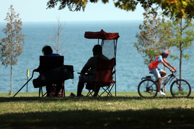 People relax in the shade as a cyclist rides by at Burnham Park in Chicago with the region under an excessive heat warning on Monday, Aug. 26, 2024. (Terrence Antonio James/Chicago Tribune)