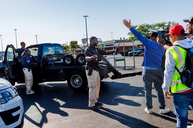 A Chicago Police officer separates a group of migrants after a tow truck driver attempted to tow a migrants vehicle while they tried to get work at the Home Depot parking lot along West 87th Street on Aug. 9, 2024, in Chicago. Migrants from all over the city visit the parking lot while looking for work. (Armando L. Sanchez/Chicago Tribune)