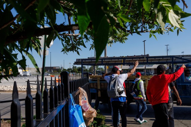 Migrants stand on the sidewalk while attempting to get work in the Home Depot parking lot along West 87th Street on Aug. 9, 2024, in Chicago. (Armando L. Sanchez/Chicago Tribune)