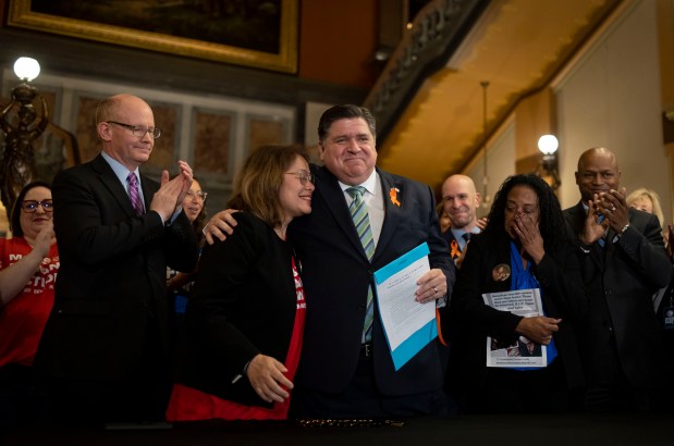 Gov. JB Pritzker hugs gun control advocate Maria Pike after he signed comprehensive legislation to ban military-style firearms on Jan. 10, 2023, at the Illinois State Capitol in Springfield. Pike and Delphine Cherry, third from right, each lost their children to gun violence. (Brian Cassella/Chicago Tribune)