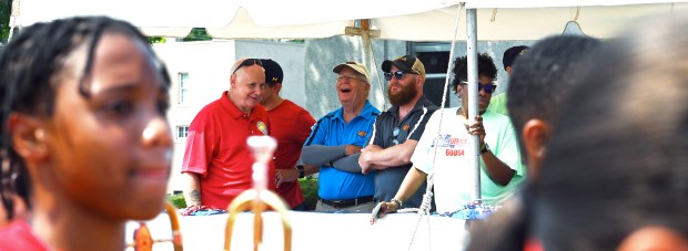 On the parade viewing stand, center, from left to right is (in Jelly Belly royal blue shirt) Bill Kelley of Winnetka, parade grand marshal and retired vice chairman of Jelly Belly, and son Brian Kelley of Northfield (in sunglasses, dark blue Jelly Belly shirt and baseball cap) at the North Chicago Community Days Parade on Aug. 3, 2024 in North Chicago. (Karie Angell Luc/Lake County News-Sun)