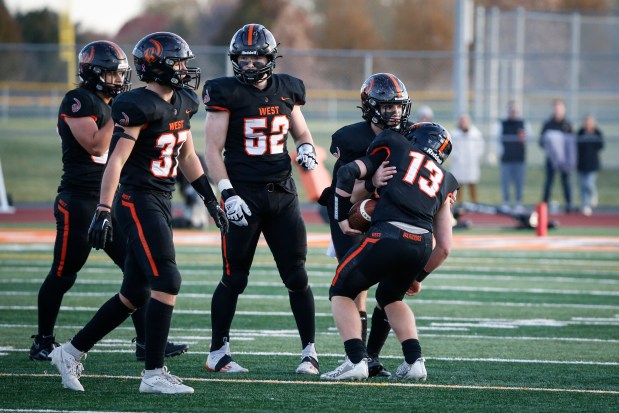 Joey Campagna (13) from Lincoln-Way West gets a little help back to his feet from quarterback Chase Hetfleisch (10) during their Class 7A state quarterfinal game against Downers Grove North on Saturday, Nov. 11, 2023 in New Lennox, Illinois. The Trojans defeated the Warriors 34-6. ( John Konstantaras-Daily Southtown ) | 3154960_ct-sta-fbl-dgn-lww-st-1113