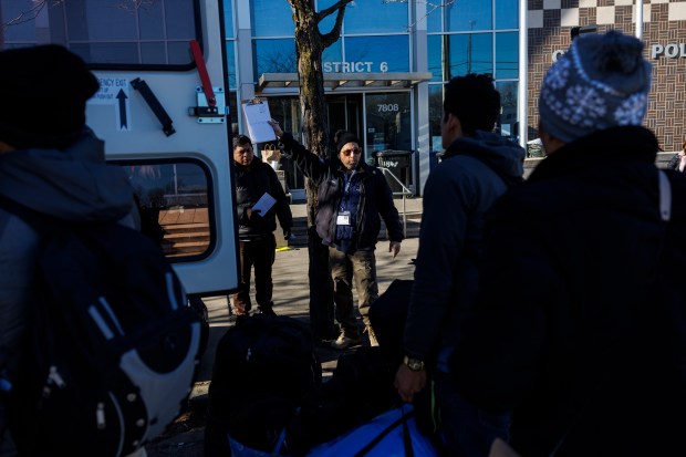 A Favorite Staffing manager, center, holds a clipboard while talking with migrants as they load belongings onto a bus outside the 6th District police station before being taken to a shelter on Dec. 13, 2023, in Chicago. (Armando L. Sanchez/Chicago Tribune)