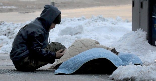 A homeless man warms his feet and legs on heat coming up through a street grate as the frigid temperatures continue in Chicago on Jan. 29, 2019. (Antonio Perez/ Chicago Tribune)