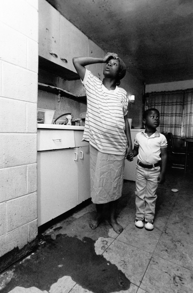 Wanda Collins and her son Christopher, 3, show where leaky pipes in their ceiling have caused constant puddles of water on the floor of their apartment on May 30, 1991, at the Henry Horner Homes in Chicago. The cabinets are also original to the building and are rusting through at 1920 W. Washington. (Chris Walker/Chicago Tribune)