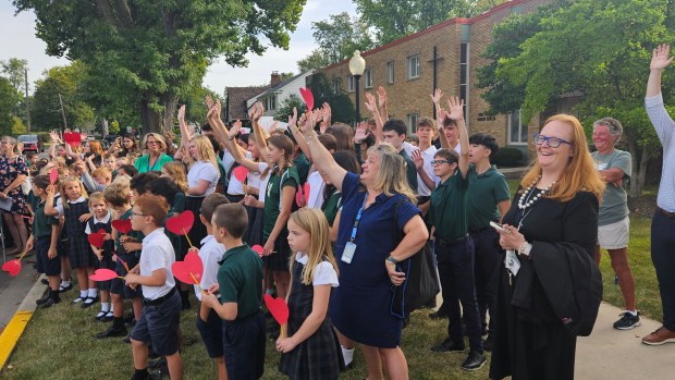 Students and staff members at Holy Angels School in Aurora raise their hands and show off heart signs made to honor former teacher Laura Waegner, who had a portion of Kensington Place renamed in her honor during a ceremony Friday morning. (David Sharos / For The Beacon-News)