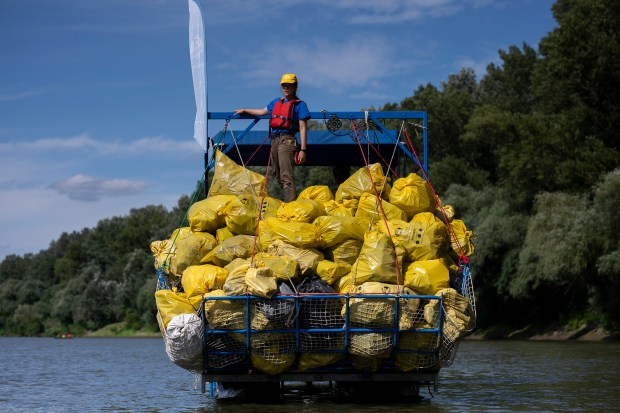 A volunteer stands on top of a pile of rubbish collected that day while participating in the Plastic Cup event near Tiszaroff, Hungary, Aug. 2, 2023. (AP Photo/Denes Erdos, File)