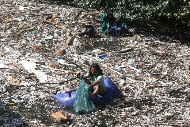 A volunteer picks up trash on a river which is covered with trash at Pecatu, Bali, Indonesia, March 22, 2024. (AP Photo/Firdia Lisnawati, File)