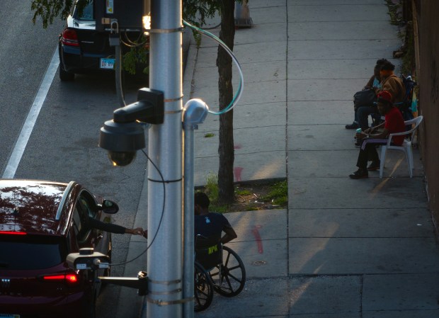 A POD camera hangs overhead as a person in a wheelchair interacts with someone in a stopped car at West Chicago and North Ridgeway avenues in Humboldt Park in July. (E. Jason Wambsgans/Chicago Tribune)