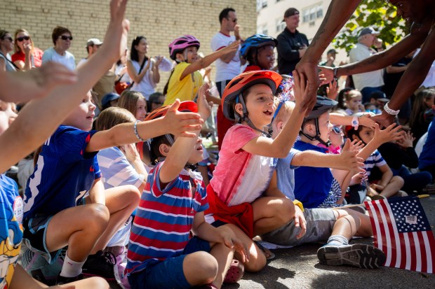 Children high-five members of the Jesse White Tumbling Team after they performed at the WOOGMS parade, short for the Wellington/Oakdale Old Glory Marching Society, in the Lakeview neighborhood of Chicago on Sept. 2, 2024. (Tess Crowley/Chicago Tribune)