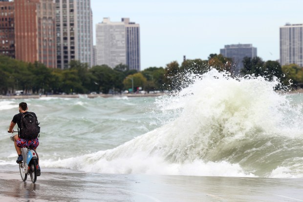 A bicyclist makes his way as strong winds create high waves across the bike and pedestrian path at 1100 N. Lake Shore Drive in Chicago, Friday, Sept. 27, 2024. (Antonio Perez/Chicago Tribune)