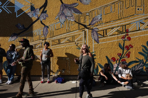 People sit and stand in front of a mosaic during the Lakeview Taco Fest in the 1300 block of West Cornelia Avenue on Saturday, Sept. 7, 2024, in Chicago. (John J. Kim/Chicago Tribune)