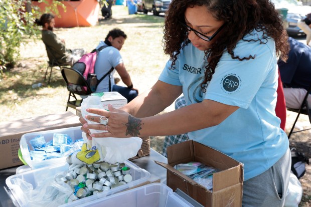 Melissa Hernandez, founder of the Puerto Rico Project, sets out boxes of syringes, caps, sterile water tubes and other supplies for victims of addiction to pick up at Humboldt Park in Chicago on Sept. 9, 2024. (Antonio Perez/Chicago Tribune)