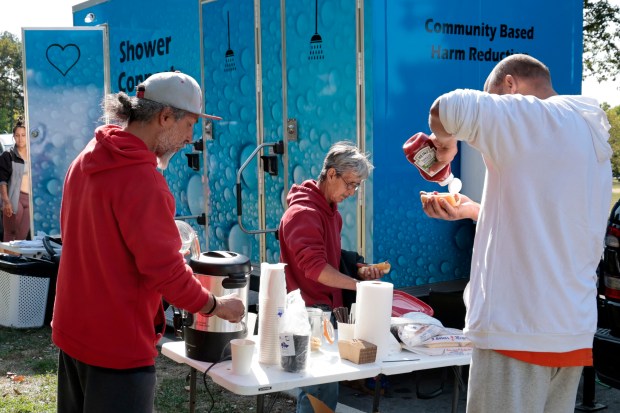 People partake of free hotdogs and coffee next to the mobile shower units in Humboldt Park in Chicago on Sept. 9, 2024. (Antonio Perez/Chicago Tribune)