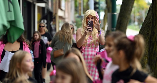 While walking with friends and family on Main Street, in Barbie clothing, is parent Morgan McConnell of Antioch taking cell phone footage at Barbie's Birthday Bash-Family Style on Sept. 28, 2024 in downtown Antioch. (Karie Angell Luc/Lake County News-Sun)