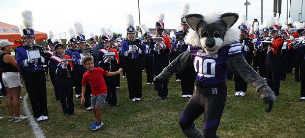 Dancing with the Northwestern University mascot Willie the Wildcat while marching band members perform is Anthony Perez, 7, an Evanston second-grader during the annual 'Kits, 'Cats & Kids Block Party on Thursday, Sep. 5, 2024 at the Evanston Township High School Lazier Field in Evanston. (Karie Angell Luc/Pioneer Press)