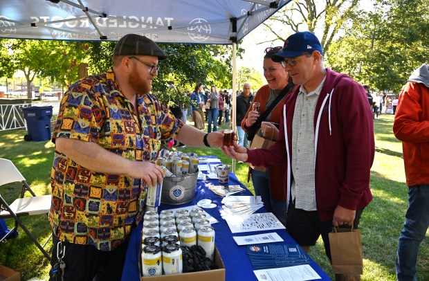 From left, Stephen MacDuffie of Rockford, service manager representing Tangled Roots Brewing Company of Glenview, offers sampling to Maureen and Mike Hominick of Edison Park during Northbrook Brewfest in Northbrook on Sept. 7, 2024. (Karie Angell Luc/Pioneer Press)