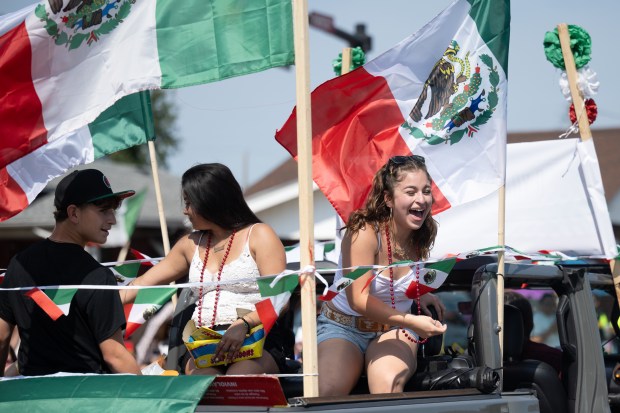 Parade participants, flying Mexican flags, throw candy from the back of trucks to paradegoers during the Fiestas Patrias Parade in East Chicago on Sunday, Sept. 15, 2024. (Kyle Telechan/for the Post-Tribune)