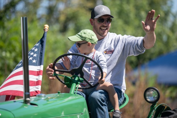 Valparaiso resident Brandon Sands and his son Stetson, 3, wave to visitors from atop a tractor as they participate in the annual Malden Labor Day parade on Monday, Sept. 2, 2024. (Kyle Telechan/for the Post-Tribune)