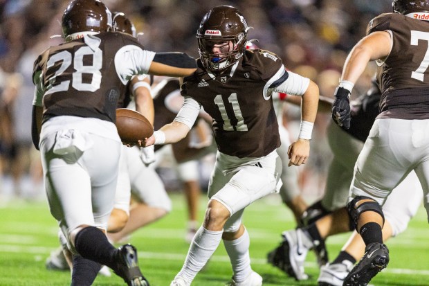 Joliet Catholic's Lucas Simulick (11) hands the ball off to Nate Magrini (28) during a CCL/ESCC Green game against Marist in Joliet on Friday, Sept. 20, 2024. (Vincent D. Johnson / Daily Southtown)