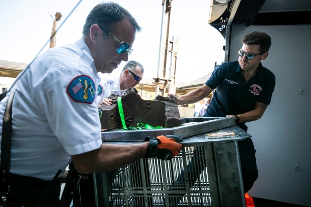 Oak Lawn firefighters Rick Sorley, from left, Eric Horkavy and Ryan Bender help reload a mobile 9/11 memorial Sept. 11, 2024, that holds a piece of the World Trade Center. The section of beam itself weighs 500 pounds and was placed back on a trailer. (Vincent D. Johnson/for the Daily Southtown)