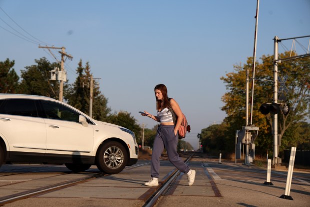 Jules Clark, a junior at Barrington High School, crosses the railroad tracks along Route 59 on Sept. 18, 2024, in Barrington. Earlier this year, 17-year-old Marin Lacson, a student at Barrington High School, was struck and killed by a train while walking to school. Community organizations want to see pedestrian gates put at this crossing. (Stacey Wescott/Chicago Tribune)