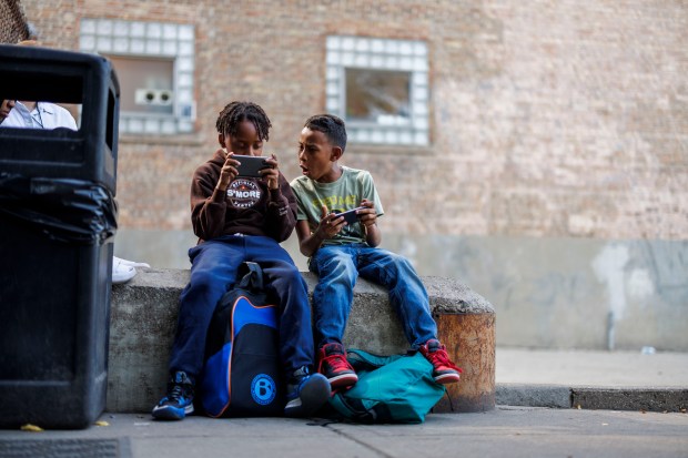 Eduardo Rodriguez, 10, left, and his brother Andres Gonzalez , 9, both from Venezuela, play with cell phones after coming home from school while sitting outside their shelter on North Ogden Avenue on Monday, Sept. 9, 2024, in Chicago. (Armando L. Sanchez/Chicago Tribune)