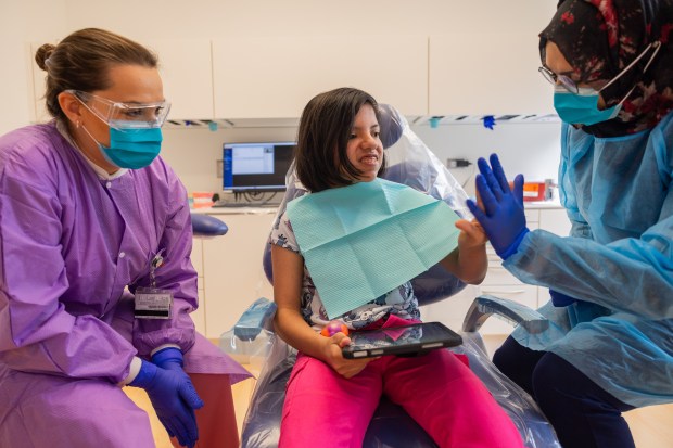 Fourth year UIC College of Dentistry student Rafia Awais, right, high-fives patient Ivanna Chavez while faculty member Renata Delgado, left, watches during a dental screening at UIC College of Dentistry's Inclusive Care Clinic in Chicago on Aug. 28, 2024. (Tess Crowley/Chicago Tribune)