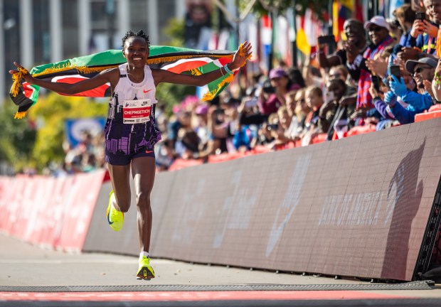 Ruth Chepngetich, from Kenya, runs with the Kenyan flag after crossing the finish line of the Chicago Marathon to win the women's professional division and break the women's marathon world record on Oct. 13, 2024. (Tess Crowley/Chicago Tribune)