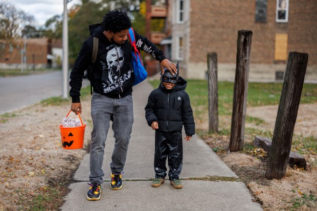 Mike Cross puts his 6-year-old son Sammy Wilson's Batman mask on while trick-or-treating in the Englewood neighborhood on Oct. 31, 2024. (Armando L. Sanchez/Chicago Tribune)