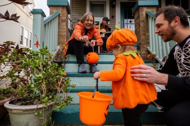 Kathy Sellman hands candy to a trick-or-treater as Chris Krall plays music in the background on Halloween in the Roscoe Village neighborhood of Chicago on Oct. 31, 2024. (Tess Crowley/Chicago Tribune)