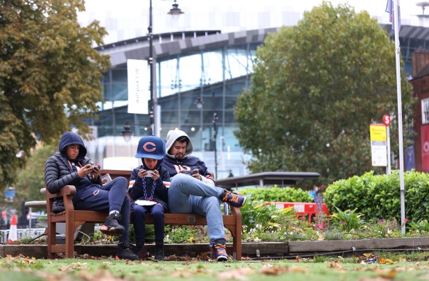 Mateo Velazquez (cq) (right) and his two sons, Sebastian (cq) (left), 14, and Santiago (cq), 9, relax on their screens outside of Tottenham Hotspur Stadium in London before a game between the Chicago Bears and the Jacksonville Jaguars on Oct. 13, 2024.  The Velazquez family lives in Chicago's Pilsen neighborhood.  (Chris Sweda/Chicago Tribune)